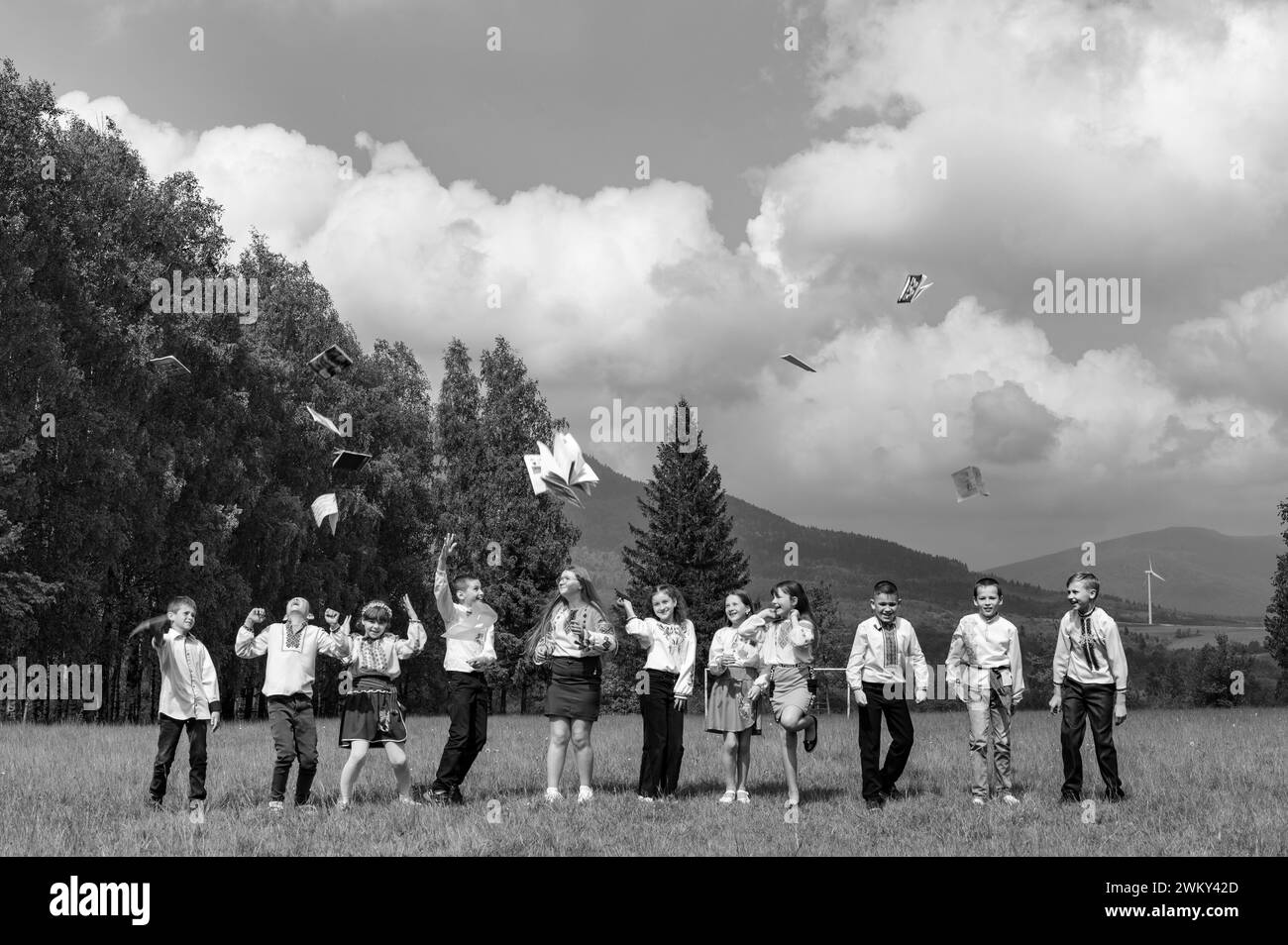 Ivano-Frankivsk, Ukraine May 26, 2023: a group of young schoolchildren throw their notebooks up, mountains and forest in the background. Stock Photo