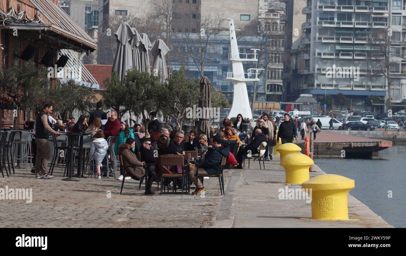 Cool breeze and sips . People  drinking coffee by the aegean sea. Yellow maritime bitts. Stock Photo