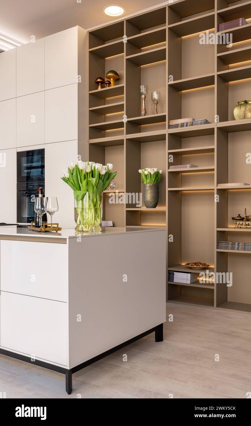 A modern, chic kitchen featuring stylish white cabinets, kitchen island and illuminated shelves Stock Photo