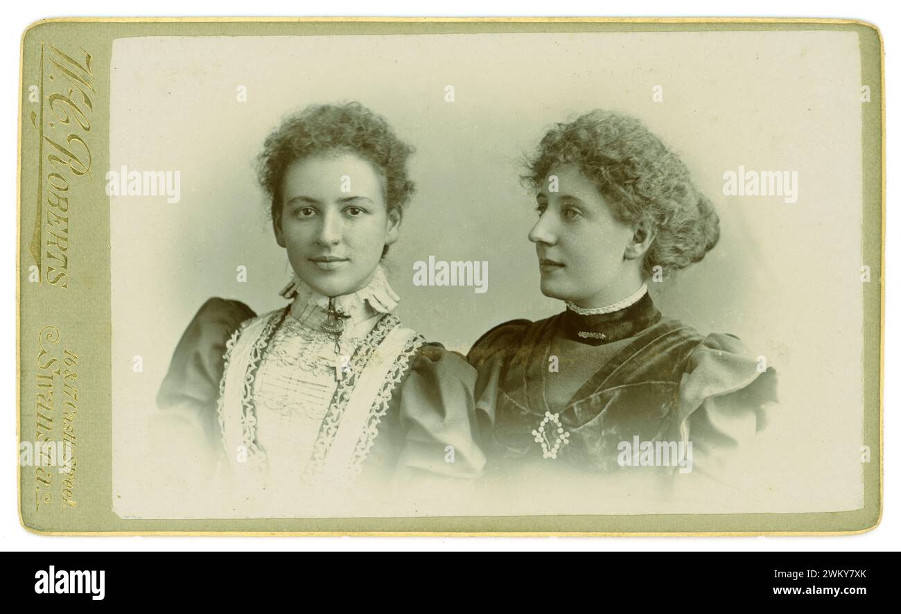 Original Victorian Carte de Visite (visiting card or CDV) of two beautiful sisters or cousins, friends, strong looking feminist feminists women, wearing fashionable dresses with puff sleeves frizzed / crimped curly hair fashionable at this time, brooches.  One of the girls looks confidently directly into the camera lens, the other is in profile. From the studio of W C Roberts 16 17 Castle St. Swansea, Wales, U.K. Circa 1897. Stock Photo