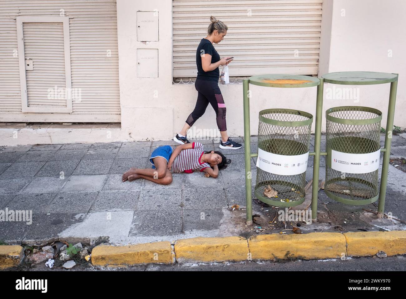 A woman walks past a child sleeping on the pavement in the Paraguayan capital, Asuncion. Picture date: Thursday February 22, 2024. Stock Photo