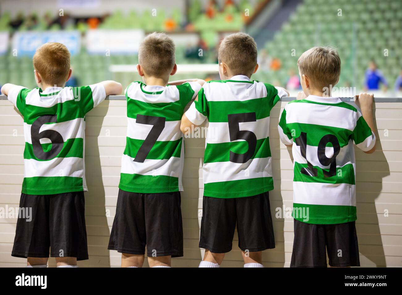 Group of children soccer players in striped jersey uniforms watching school tournament match. Football game for kids. Kids soccer teammates standing t Stock Photo