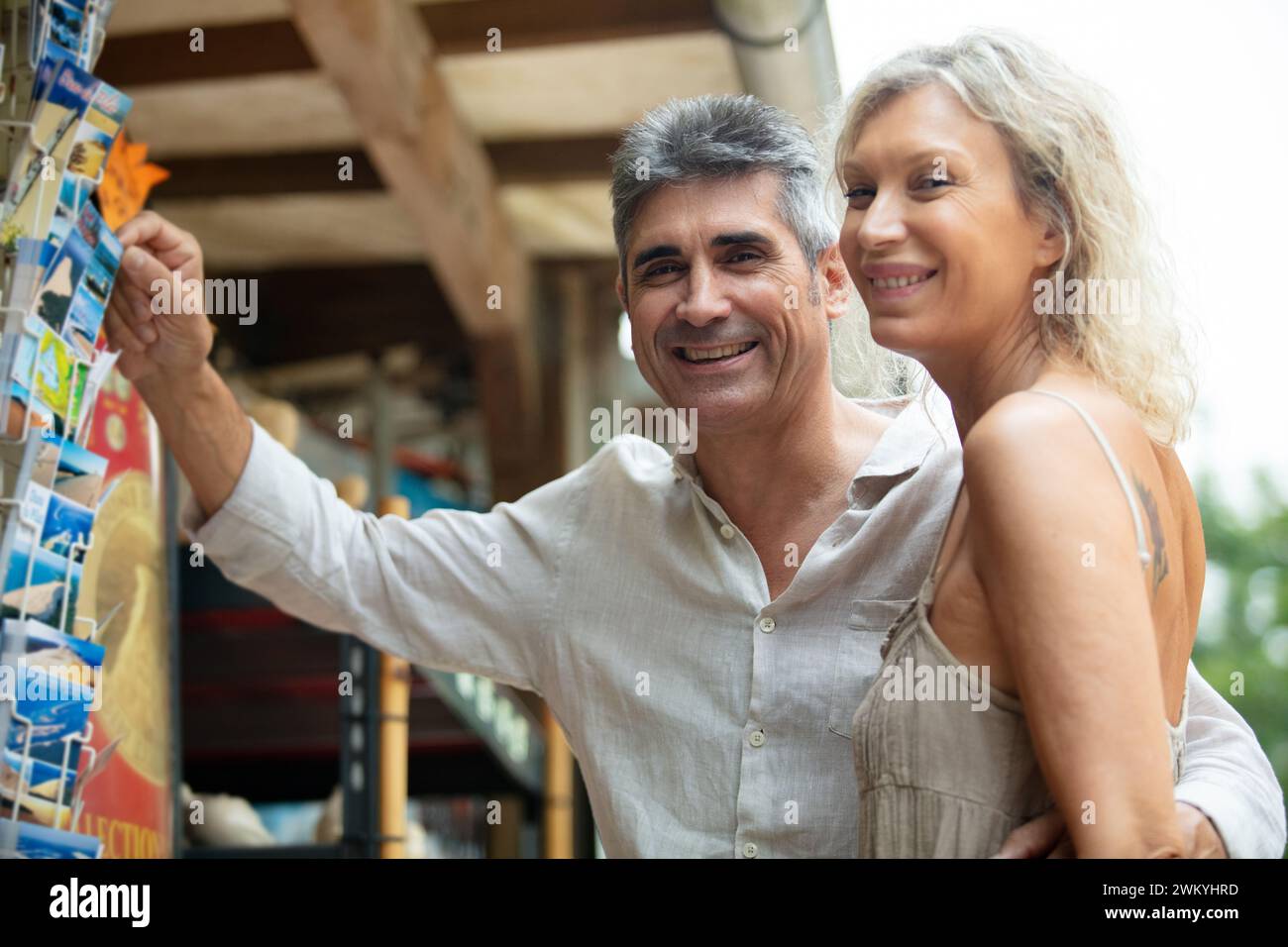 a middle-aged couple looking at postcards outside a souvenir shop Stock Photo