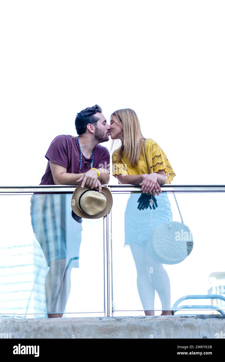High above the city, a couple shares a tender moment, their kiss framed by the open sky. The man holds his straw hat, adding a playful touch to the sc Stock Photo