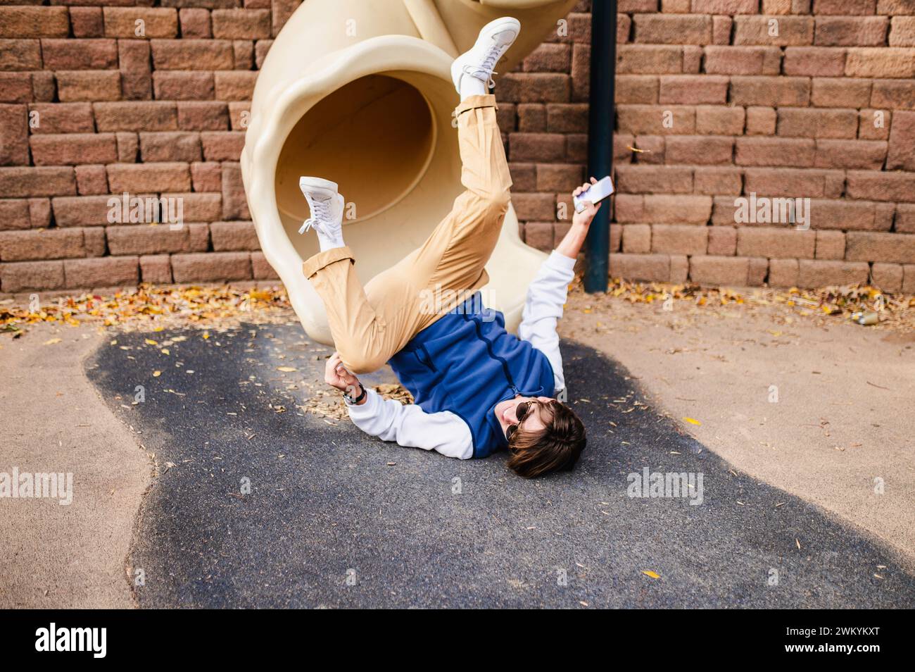Teenager playfully falling from slide Stock Photo