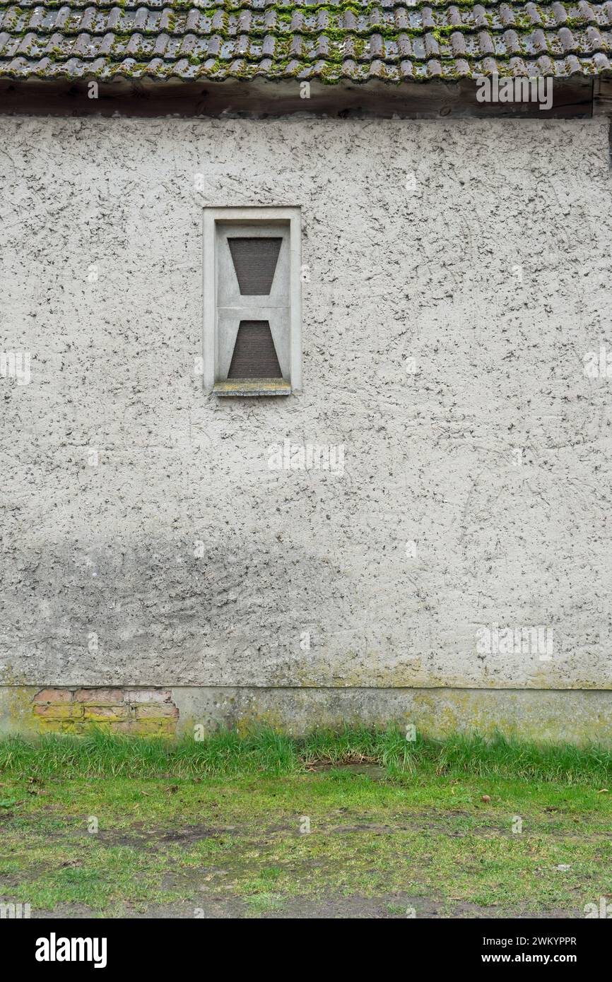 Gray exterior wall with washed plaster and a small window made of glass blocks Stock Photo