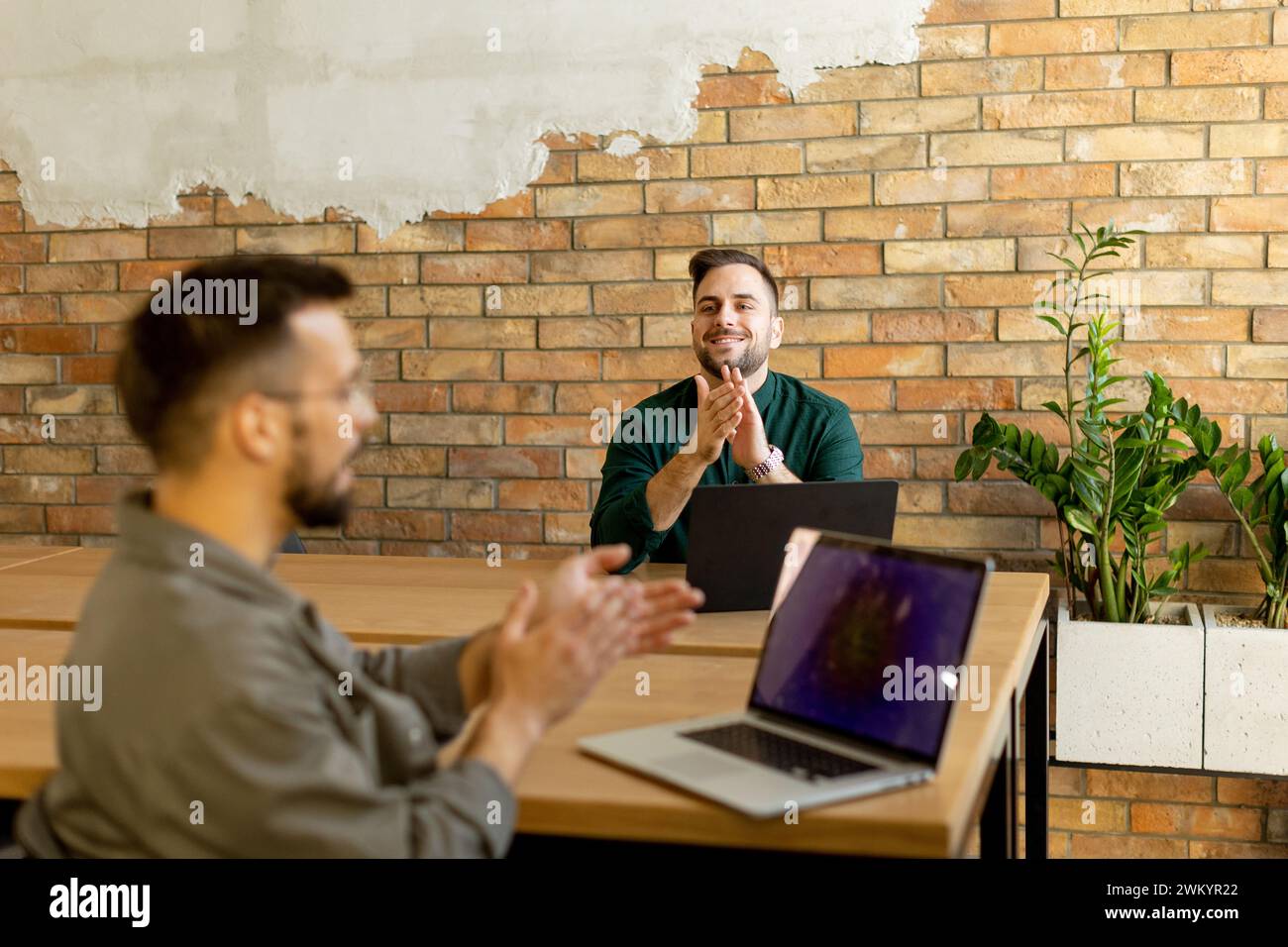 Two smiling professionals engage in a collaborative work session at a wooden table, their camaraderie evident in a contemporary office setting with an Stock Photo
