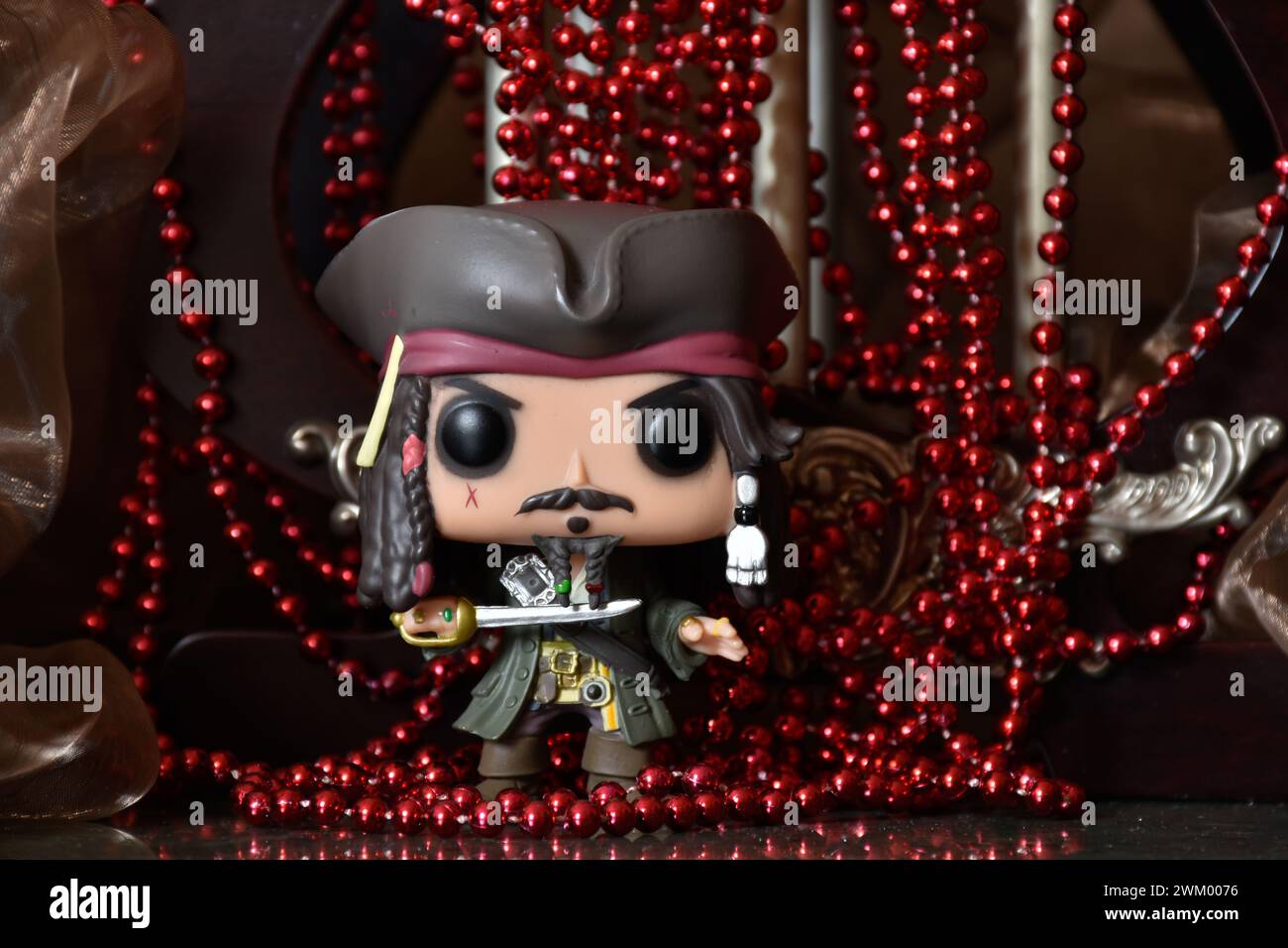 Funko Pop action figure of captain Jack Sparrow from movie Pirates of the Caribbean. Treasure, red necklace, cocked hat, sword, cave, dark palace. Stock Photo