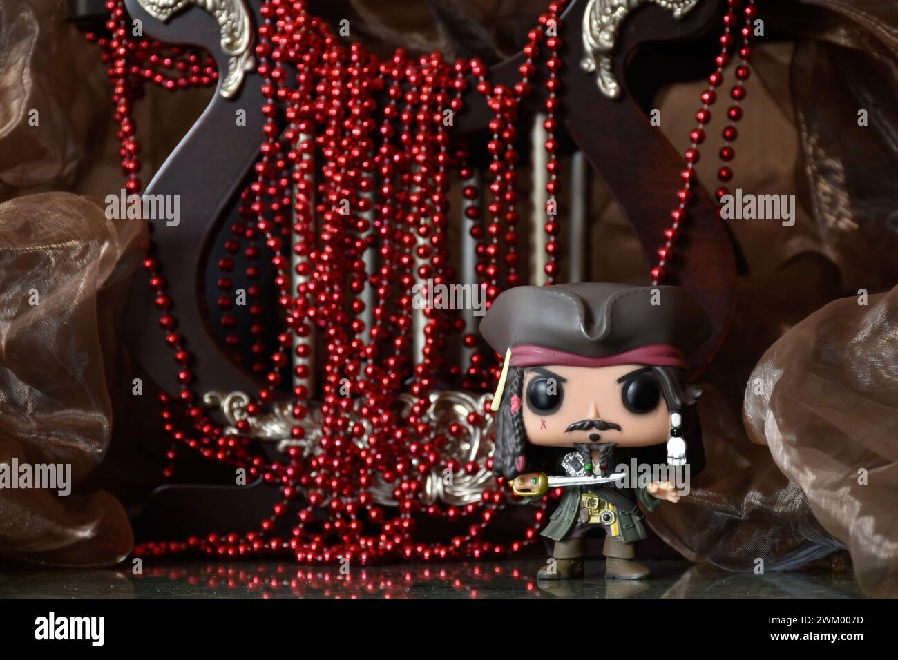 Funko Pop action figure of captain Jack Sparrow from movie Pirates of the Caribbean. Treasure, red necklace, cocked hat, sword, cave, dark palace. Stock Photo