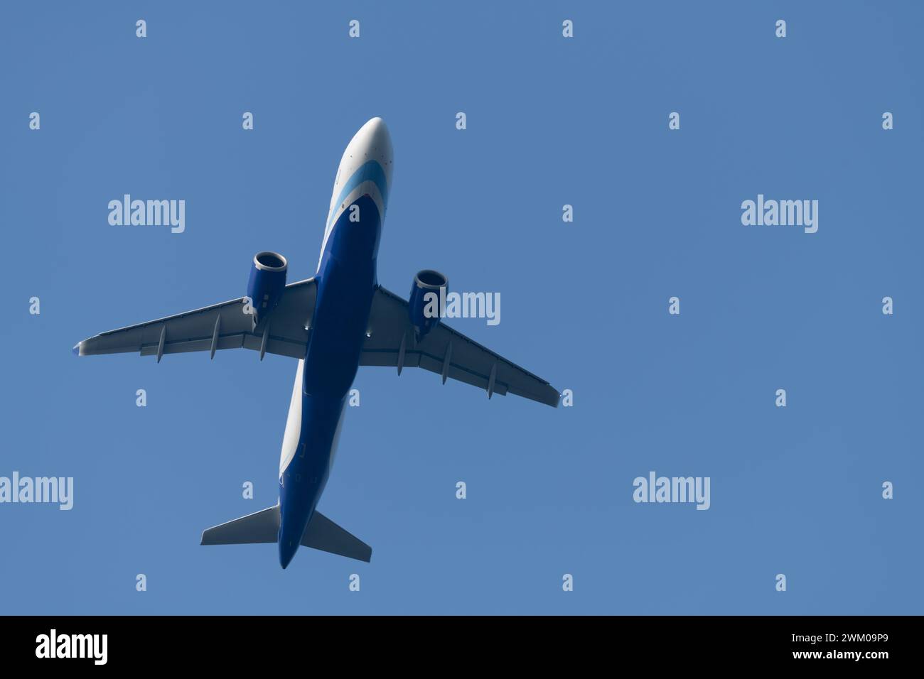 Underside of a commercial jet flying overhead, an Airbus A320 Neo against a blue sky background. Stock Photo
