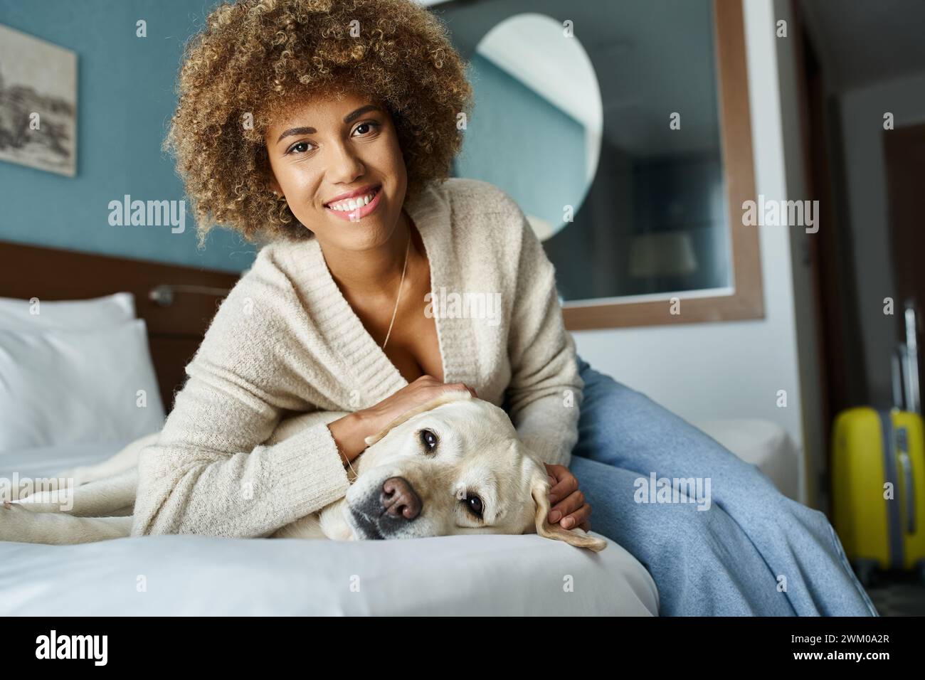 young and happy african american woman cuddling labrador on a bed in a