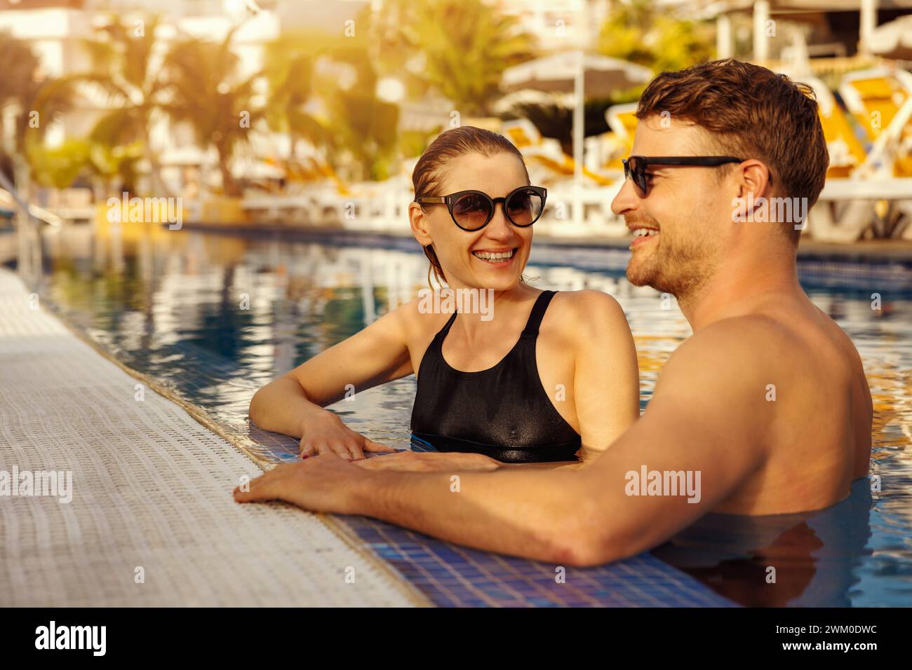 young happy couple relaxing together in tropical resort swimming pool. summer vacation, romantic getaway Stock Photo