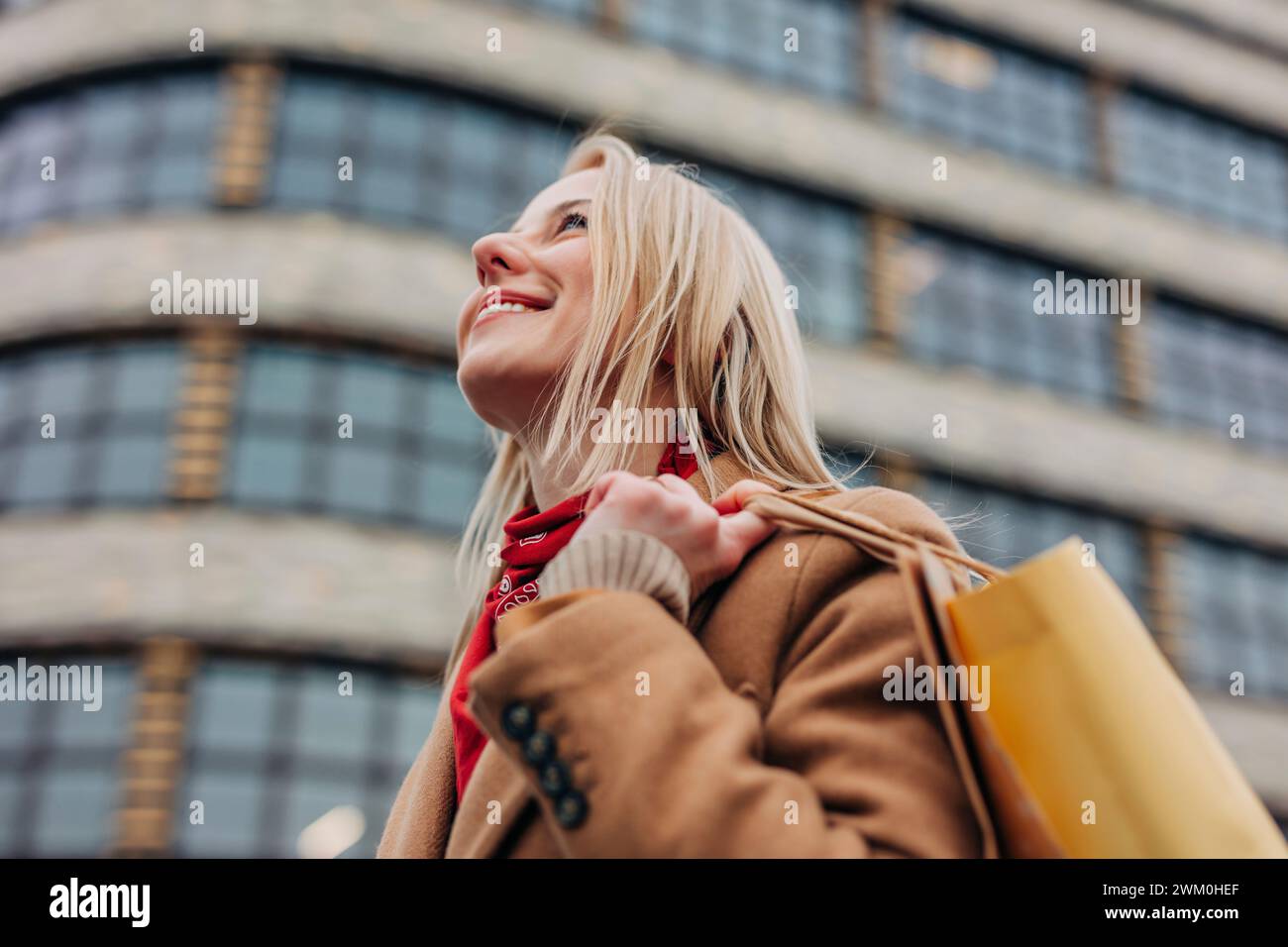 Smiling woman carrying shopping bags in front of building Stock Photo