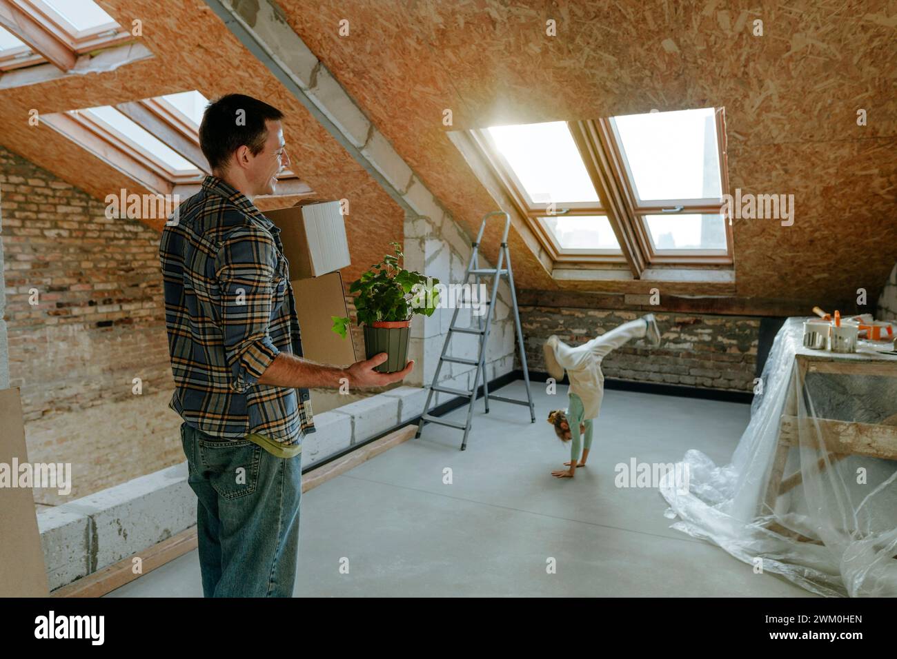 Father looking at daughter doing cartwheel in room under renovation Stock Photo