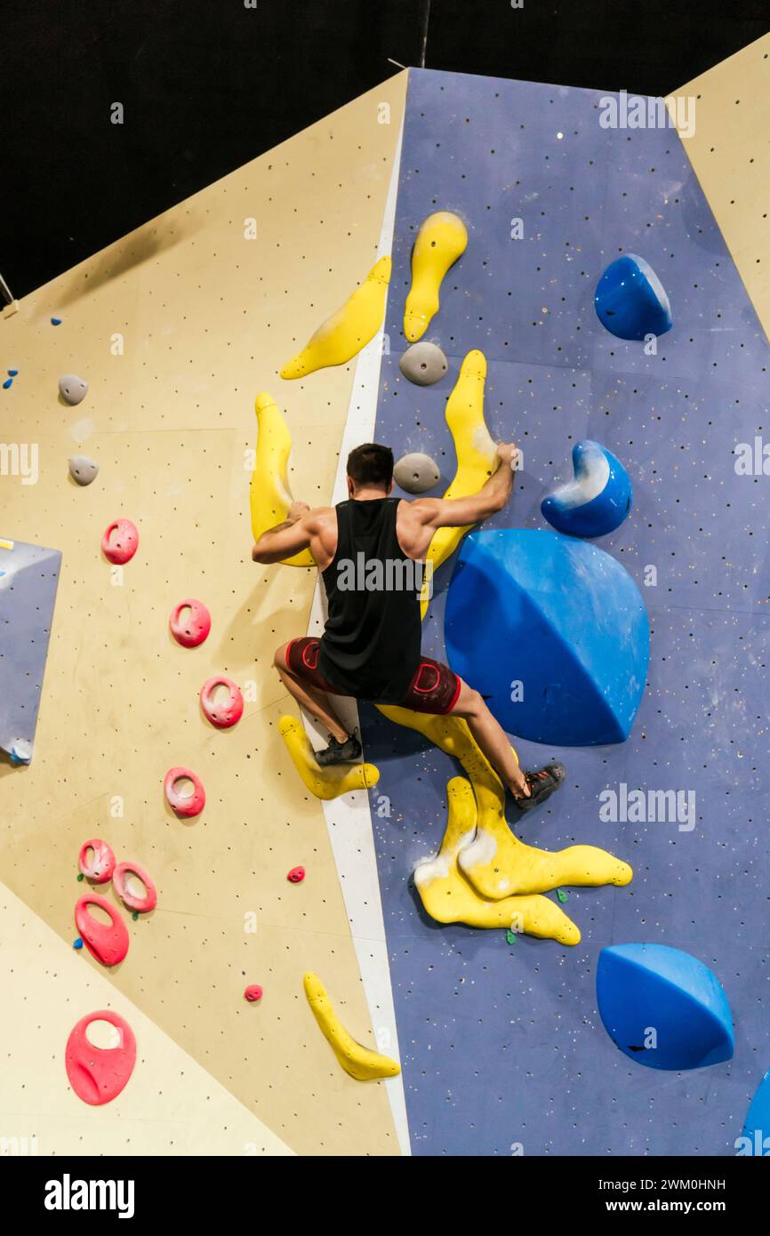 Athlete climbing on artificial bouldering wall in gym Stock Photo