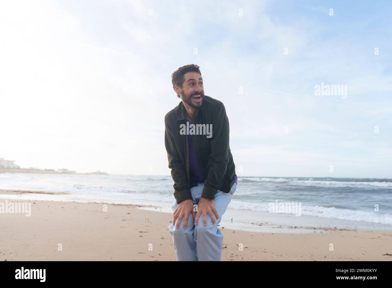 Cheerful man with hands on knees standing at beach Stock Photo