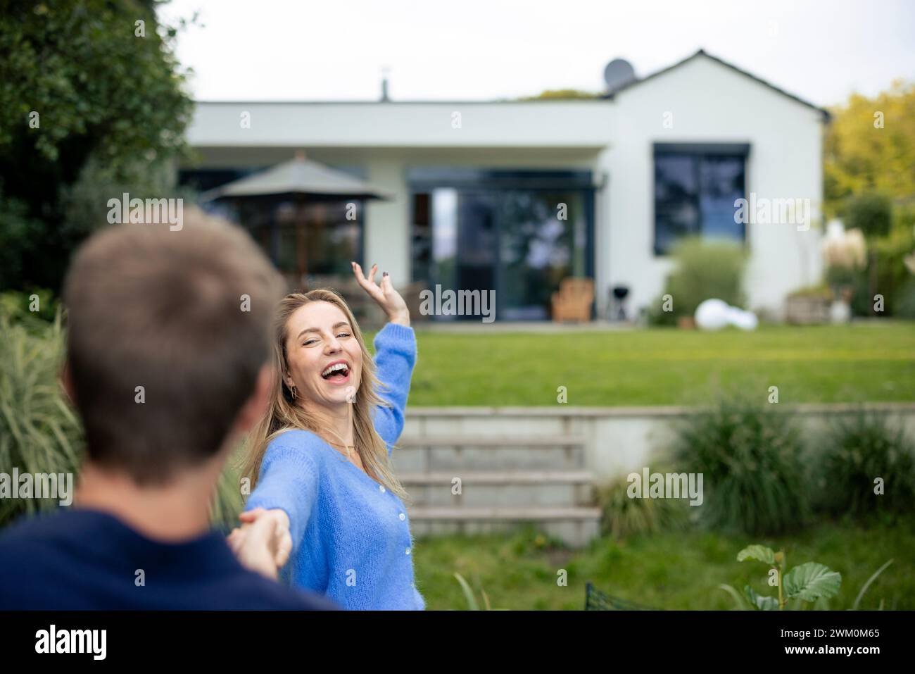 Cheerful woman holding hands with man in front of house Stock Photo