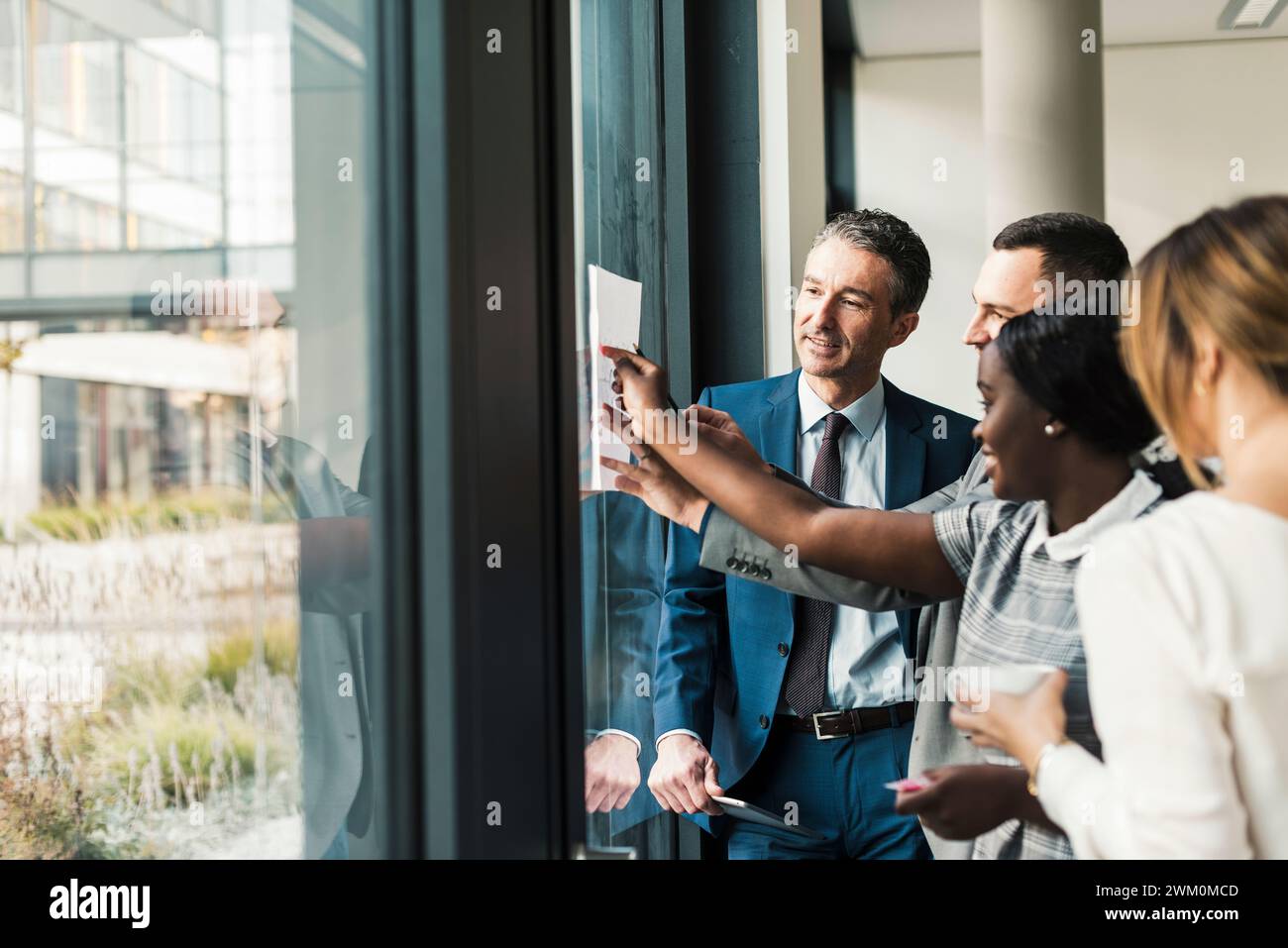 Happy business colleagues discussing over document on window at office Stock Photo