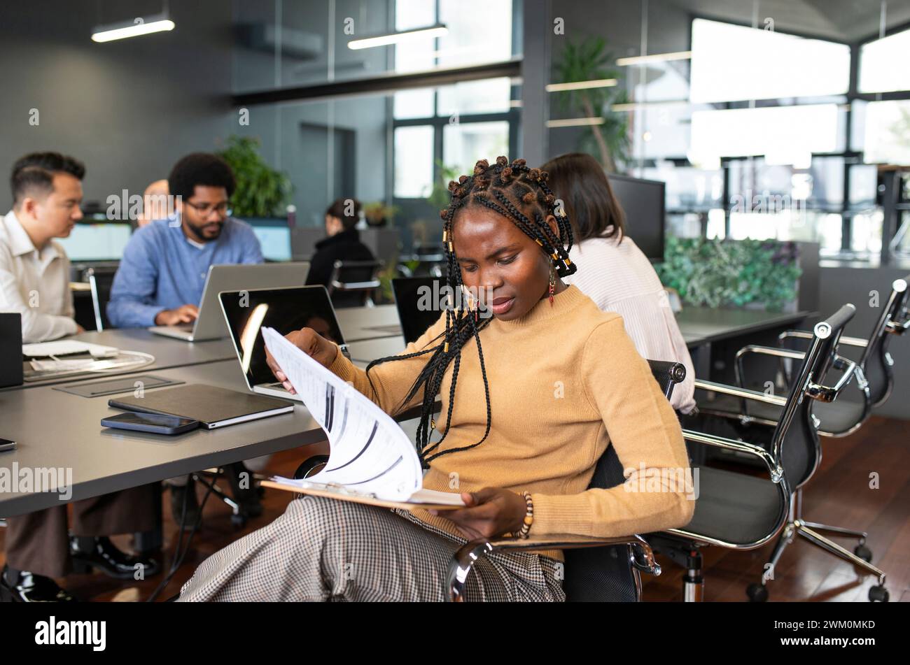 Stressed businesswoman examining documents with colleagues working in background Stock Photo