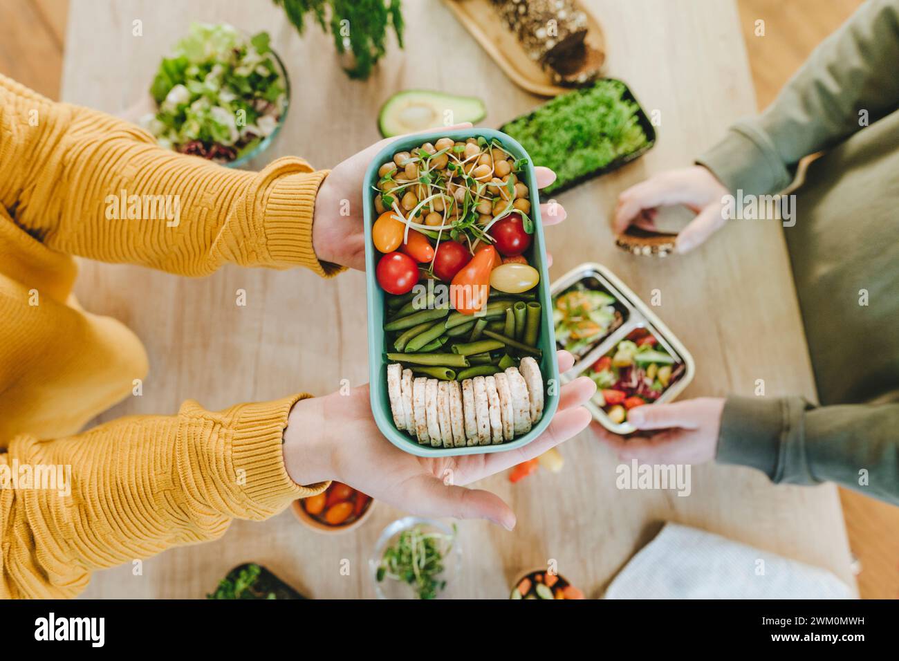 Hands of woman holding vegetarian food lunch box near man at table Stock Photo