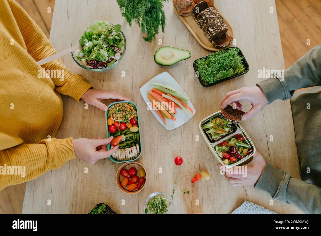 Young couple preparing food in lunch boxes at table Stock Photo