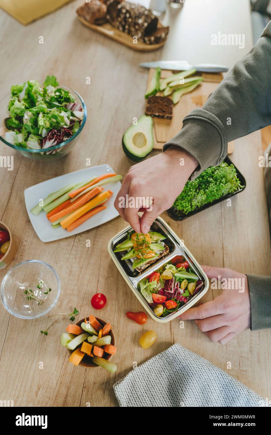 Young man garnishing microgreen over vegetarian food in lunch box Stock Photo