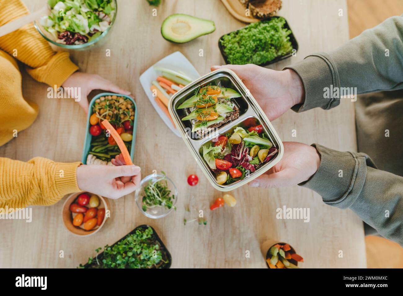 Hands of man holding vegetarian lunch box near woman at table Stock Photo