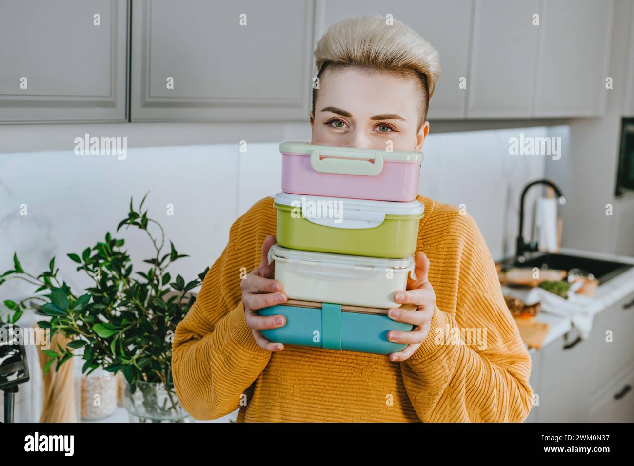 Young woman holding lunch boxes in kitchen at home Stock Photo