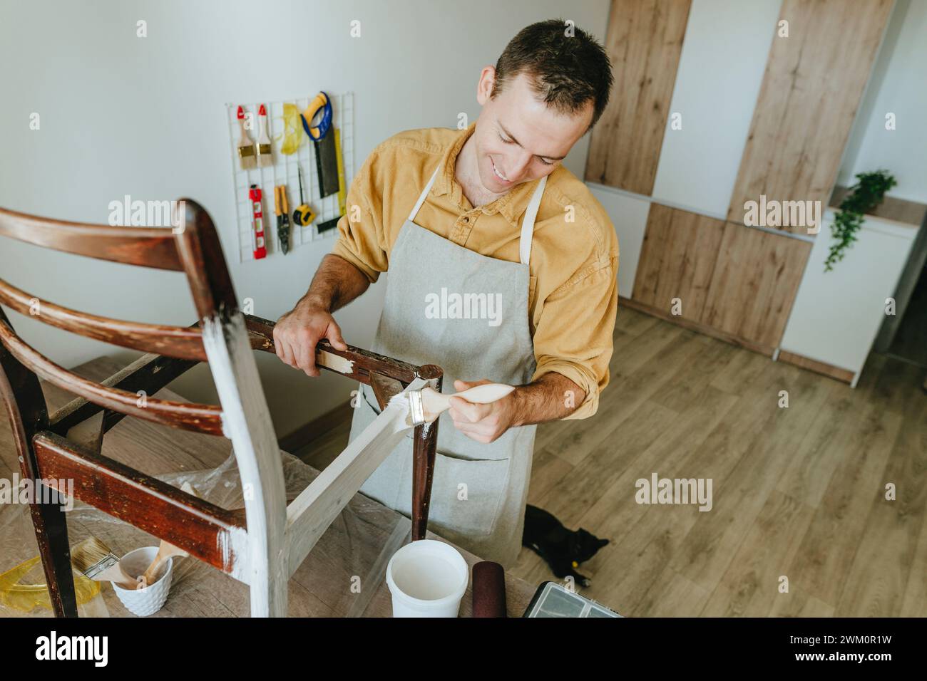 Smiling man painting chair with brush standing at home Stock Photo