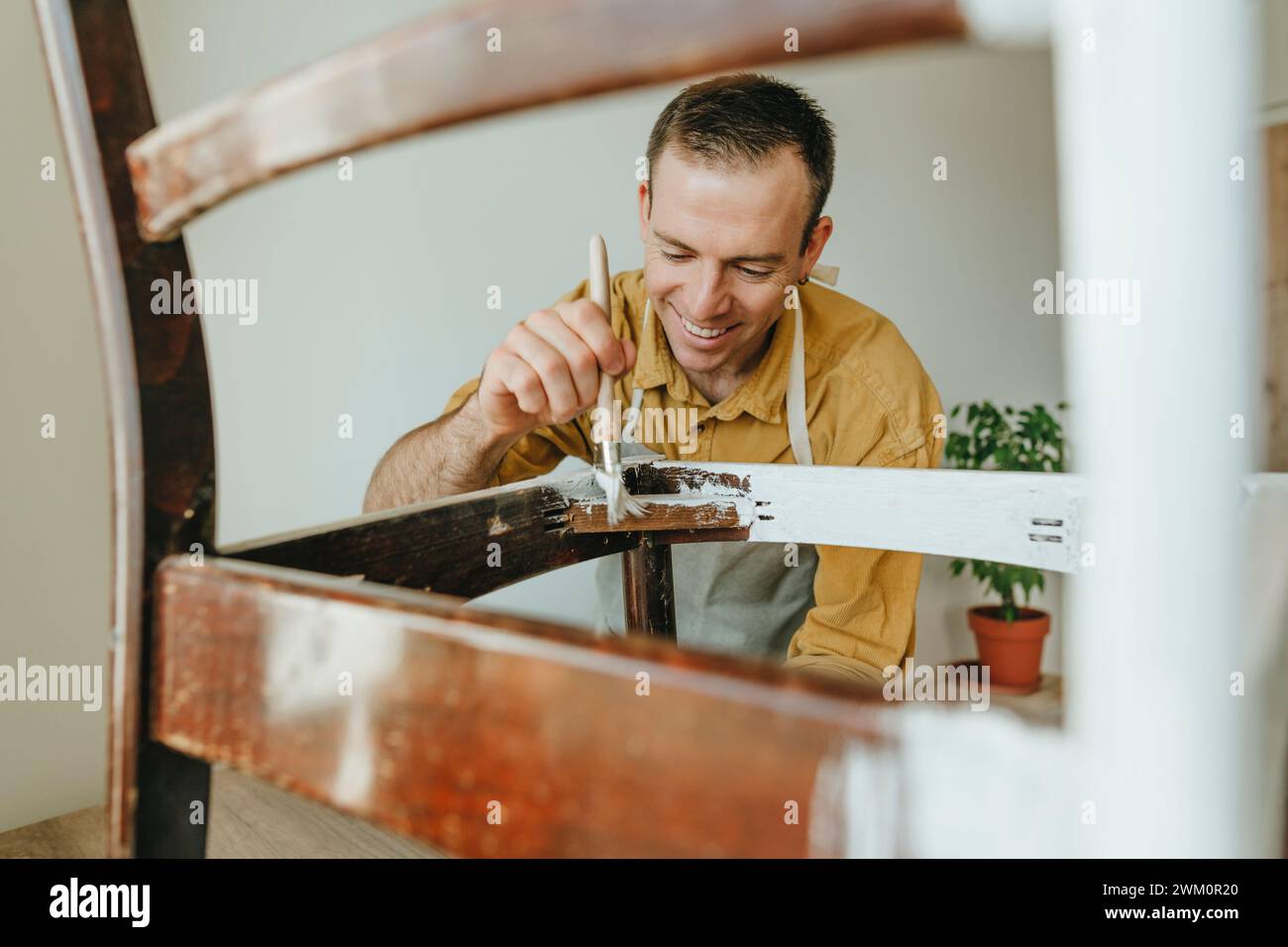 Smiling man painting white paint on chair at home Stock Photo