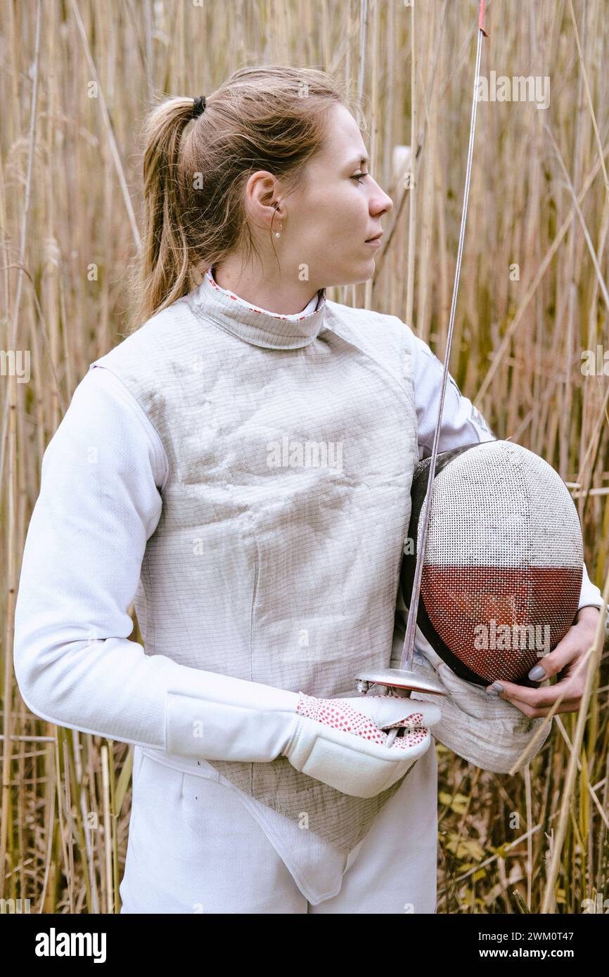 Fencer holding mask and foil standing amidst grass Stock Photo
