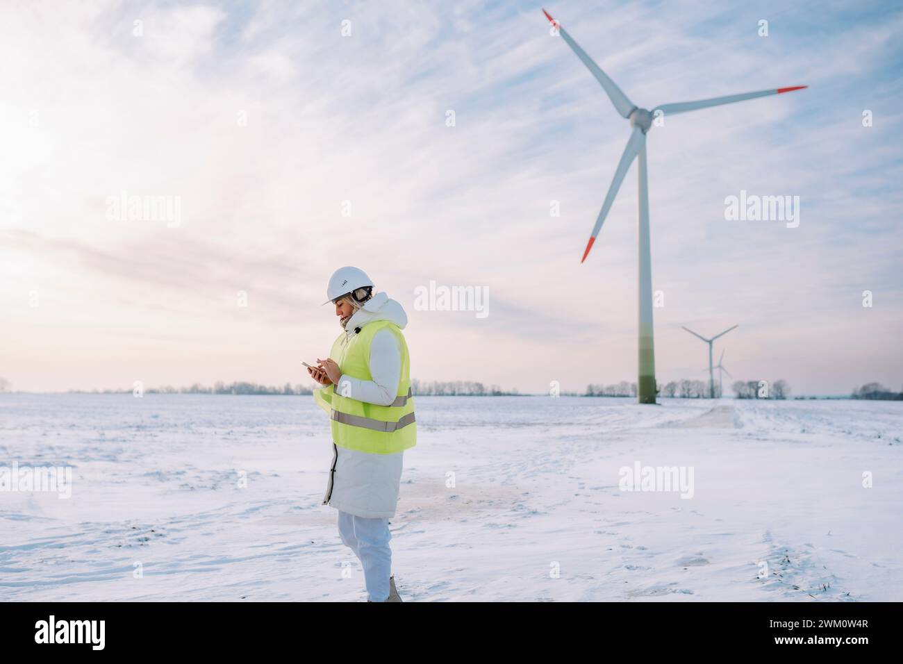Engineer using smart phone standing at wind farm Stock Photo