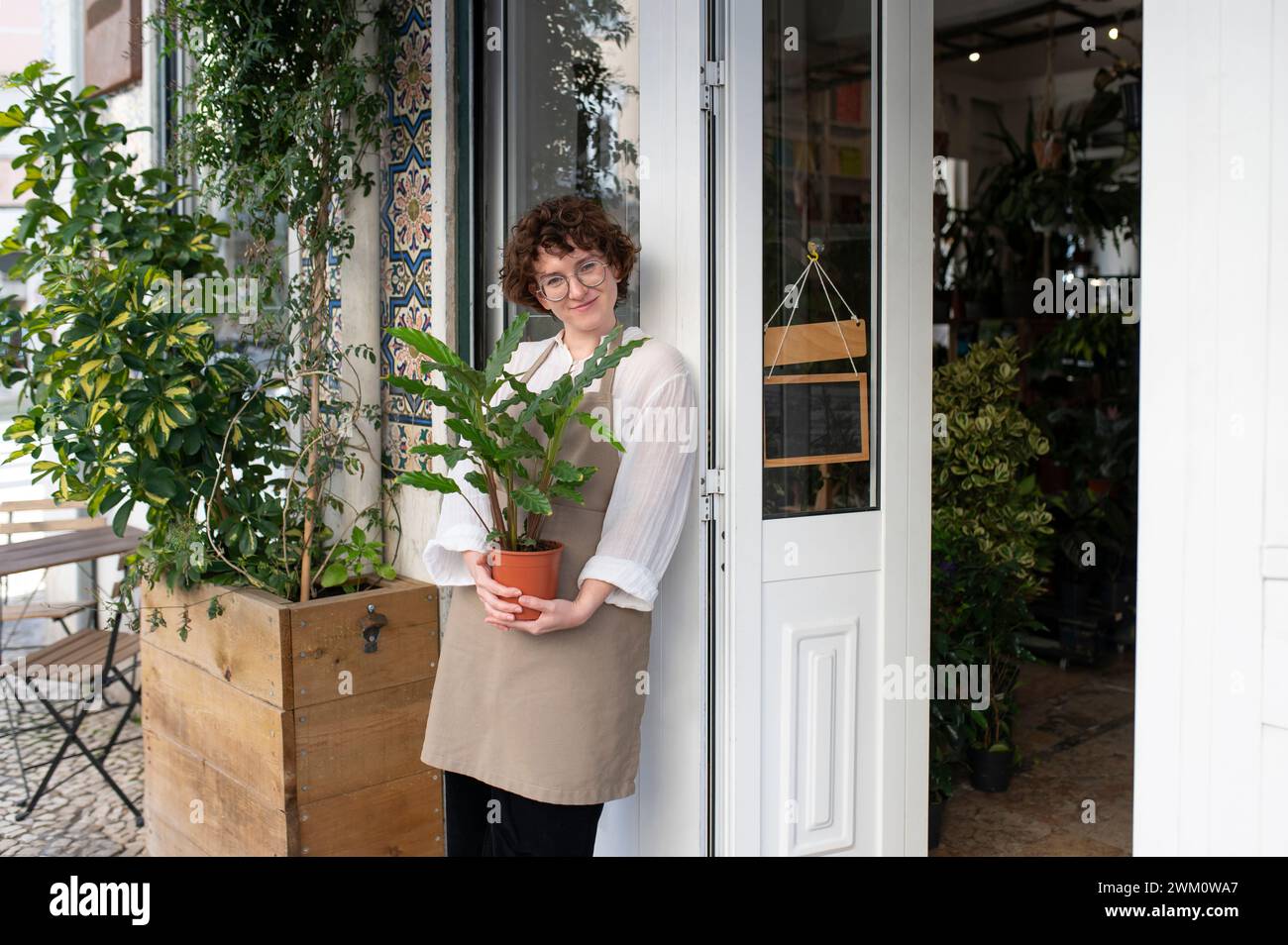 Smiling owner holding potted plant at nursery entrance Stock Photo - Alamy