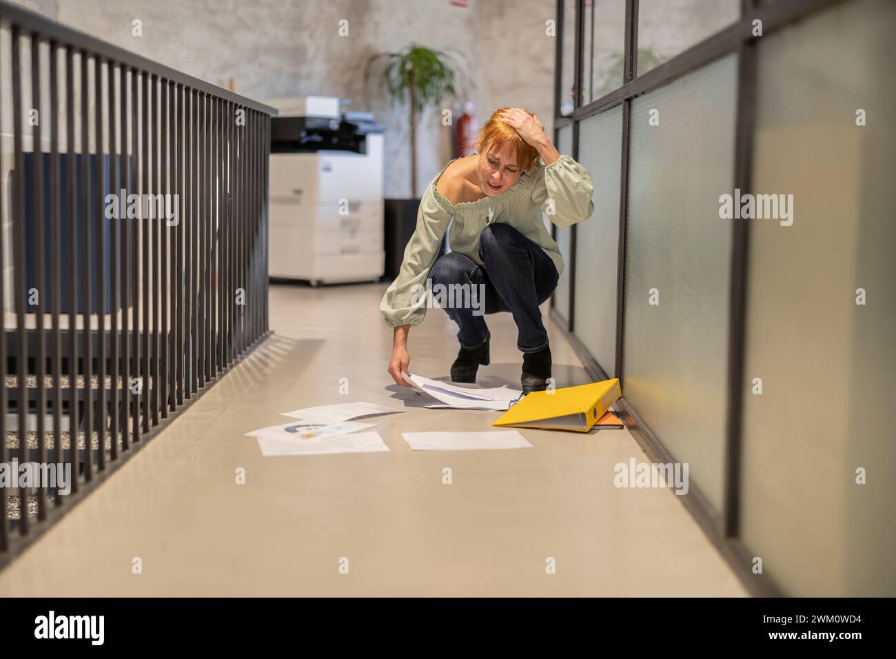 Careless mature businesswoman picking scattered documents in corridor at office Stock Photo