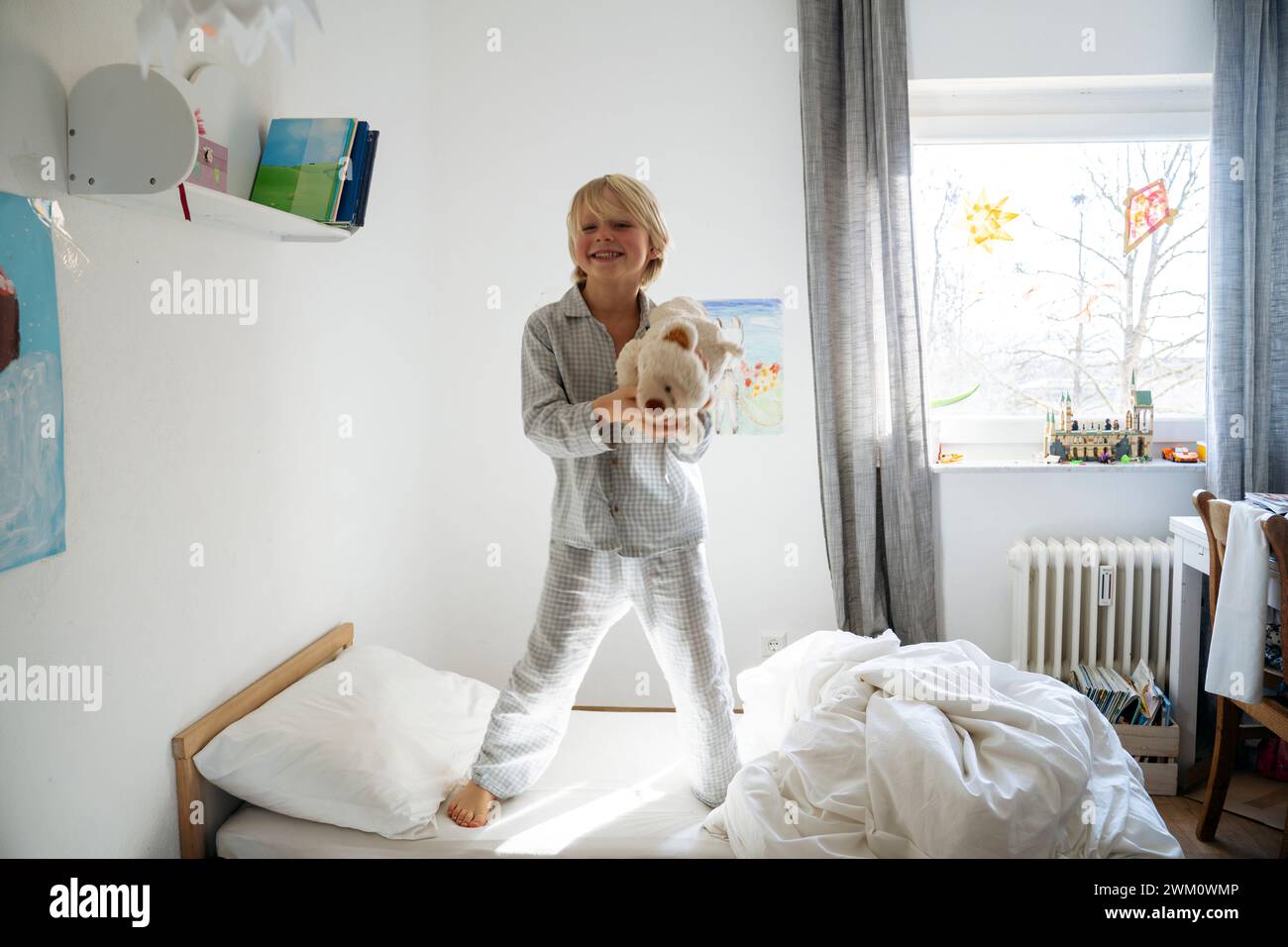Happy boy holding teddy bear and standing on bed at home Stock Photo ...