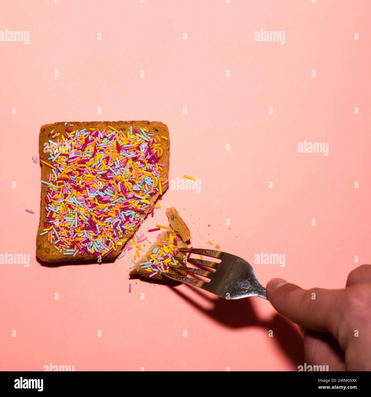 Toast with colorful sprinkles and fork on pink background. Creative food concept. Stock Photo