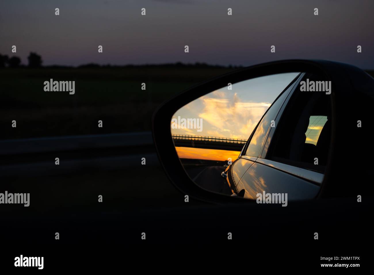 View in the outside rearview mirror of a car. View from inside of the car. Evening car ride on the highway. Stock Photo