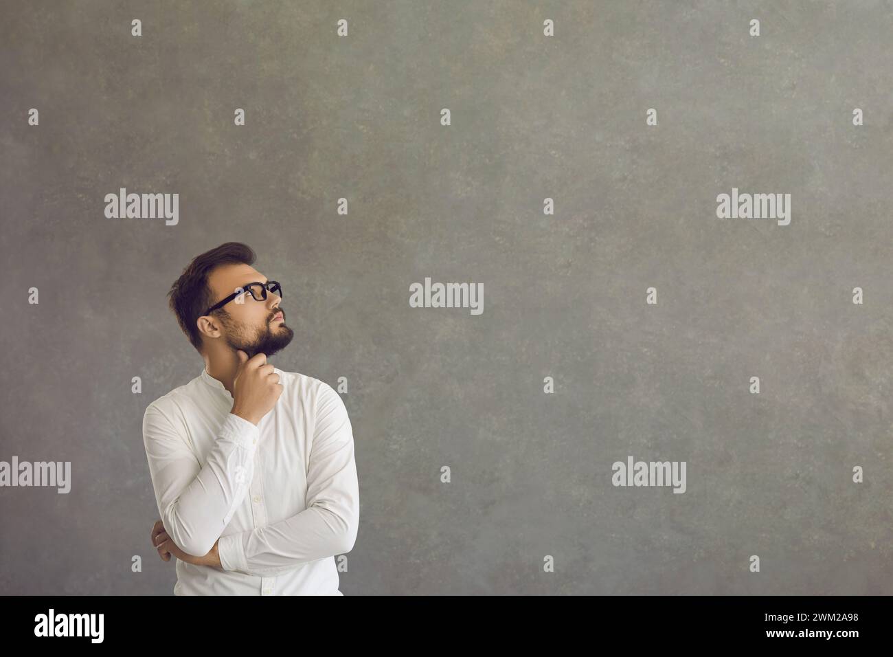 Man reflect on question or business problem looking aside standing on grey Stock Photo