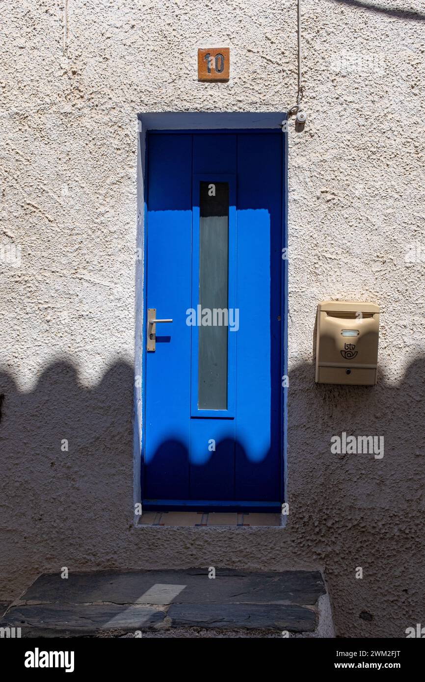 A blue door on a white wall with the shadow of roof tiles. Taken in Cadaques, Spain Stock Photo