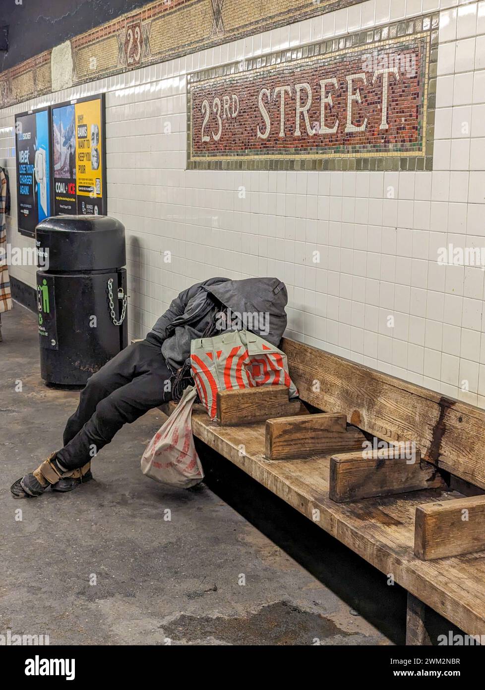 New York City, NY - February 18, 2024:  Homeless man sleeping on a bench in a subway station in New York City Stock Photo