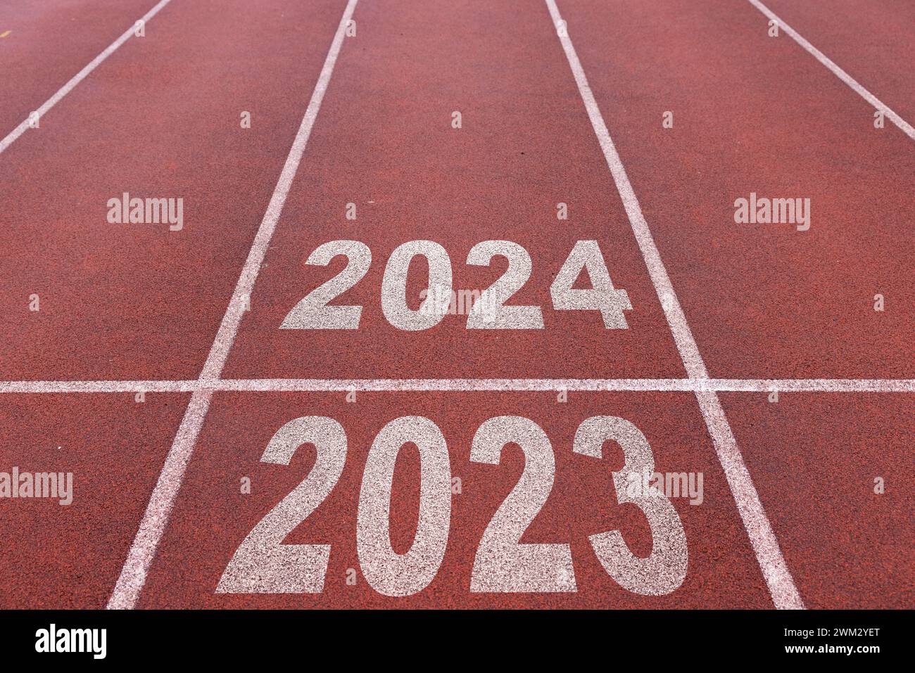 Happy new year 2024 symbolizes the start of the new year. Rear view of a man preparing to run on the athletics track engraved with the year 2024. Stock Photo