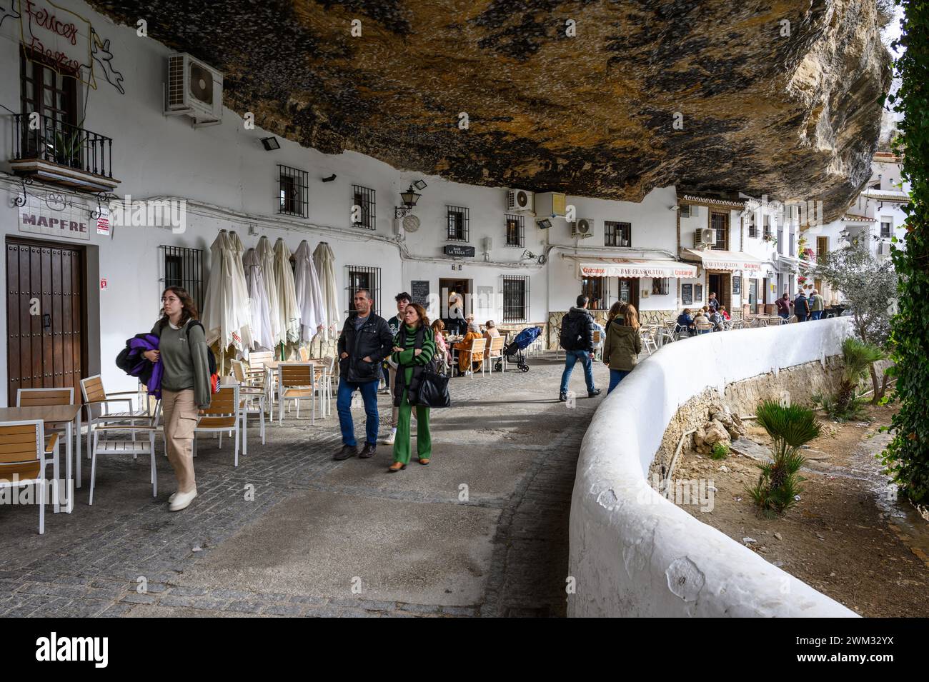 Typical street Caves of the sun in Setenil with restaurants and houses inside the rocks of the mountain and tourists walking around, Cadiz, Spain. Stock Photo