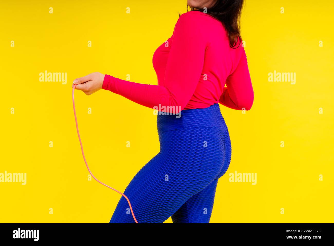 Pretty smiling plump female in sporty top and leggings holding jumping ...