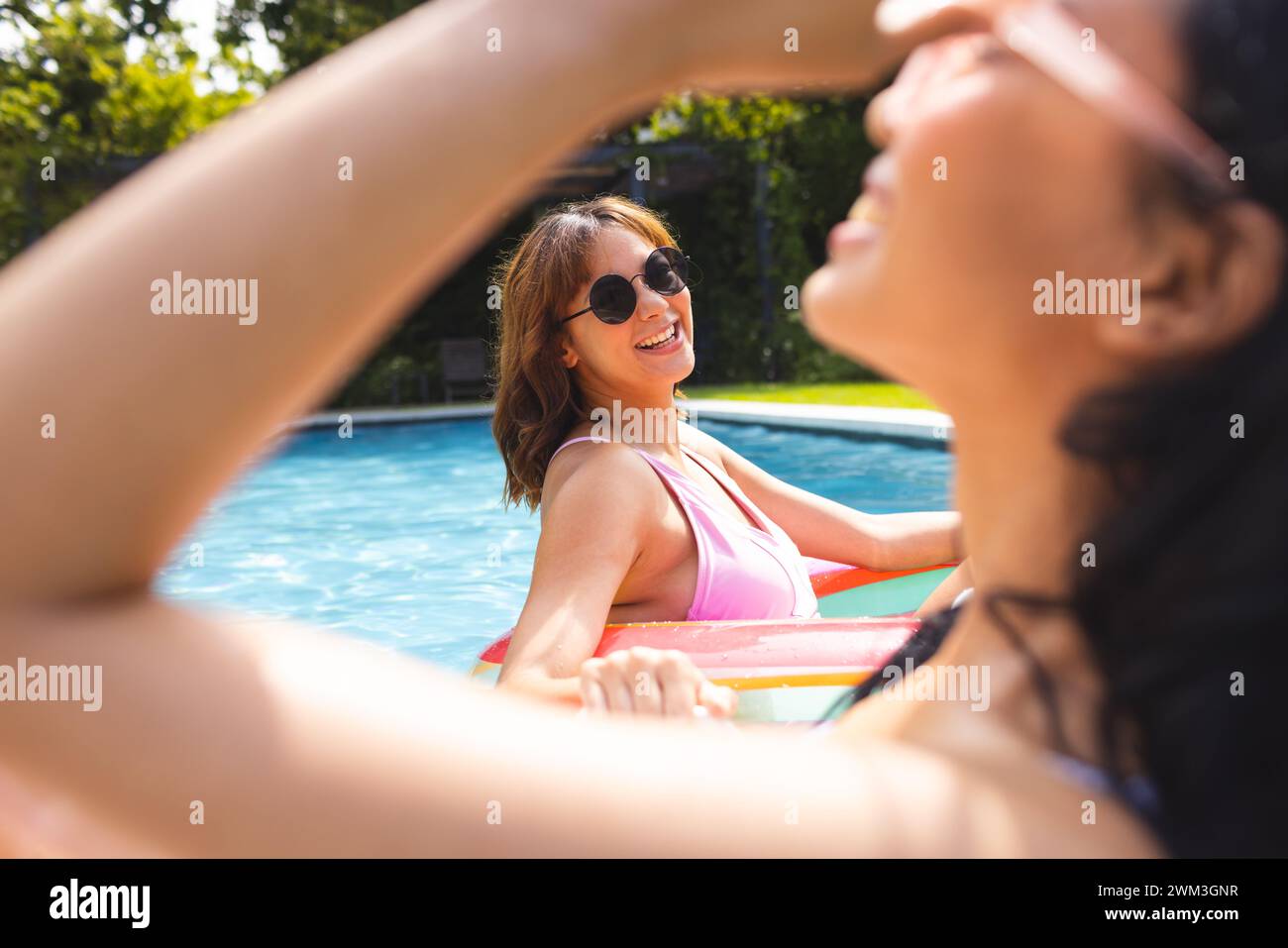 Biracial female friends enjoy a sunny day in the pool Stock Photo