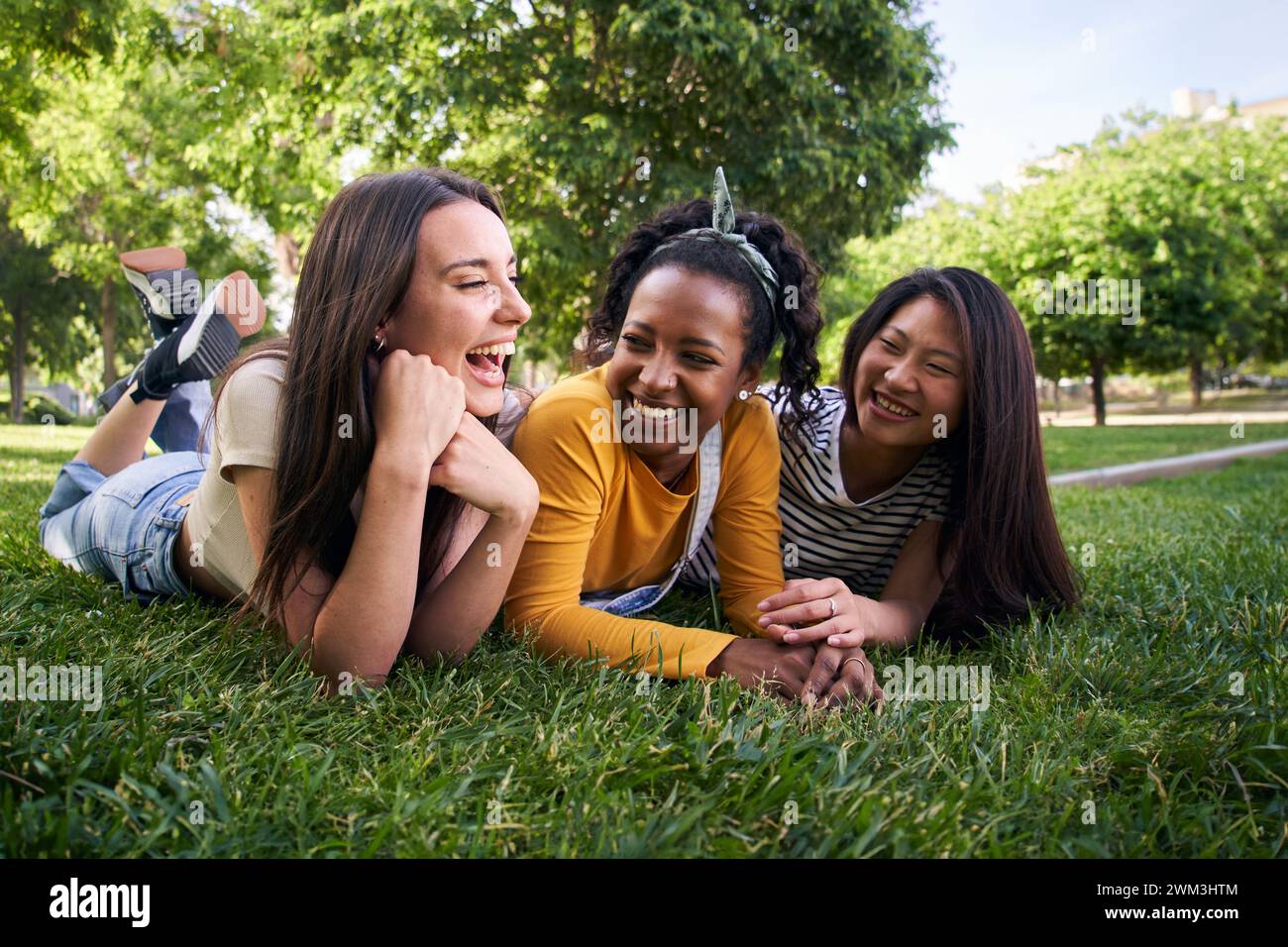 Group multiracial joyful young beautiful women laughing lying chatting having fun on grass in park. Stock Photo