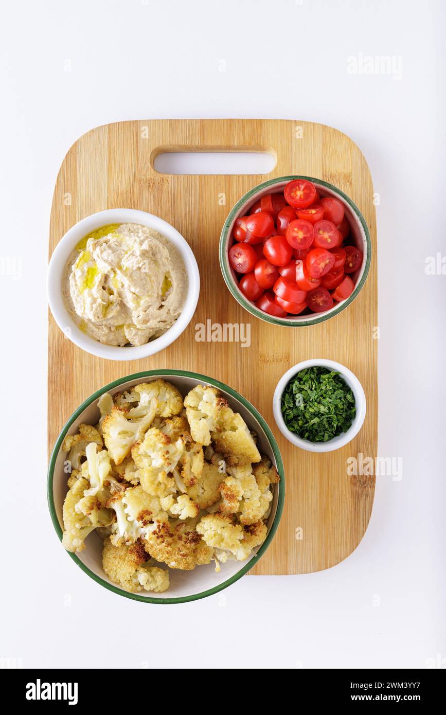Roasted cauliflower tomatoes and hummus salad ingredients on a wood cutting white background