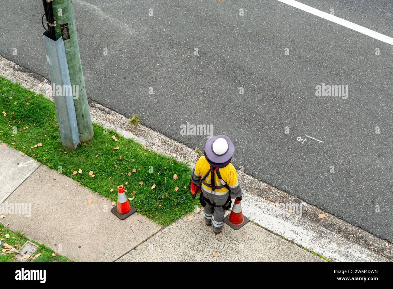 Electricity worker standing near wooden power pole on street edge. Stock Photo