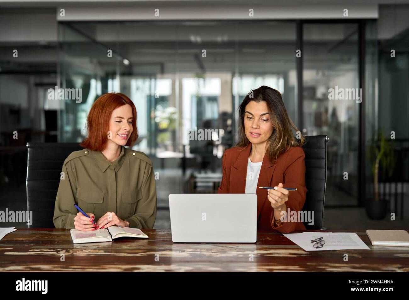 Two busy business women working together using laptop at desk in office. Stock Photo