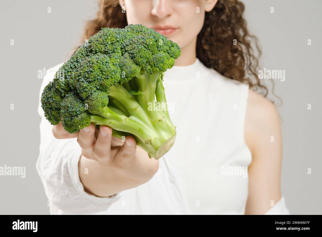 Unrecognizable woman holding broccoli in her outstretched hand, focus on foreground Stock Photo
