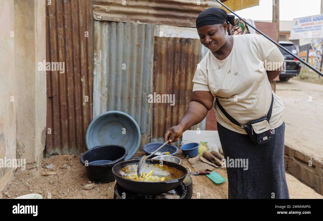 Junge Afrikanerin braet Kartoffeln fuer den Verkauf an der Strasse, Nyanya, 06.02.2024. Nyanya Nigeria *** Young African woman brewing potatoes for sa Stock Photo